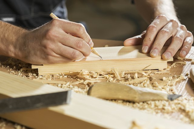 Een hand tekent met een potlood een lijn op een houten plank